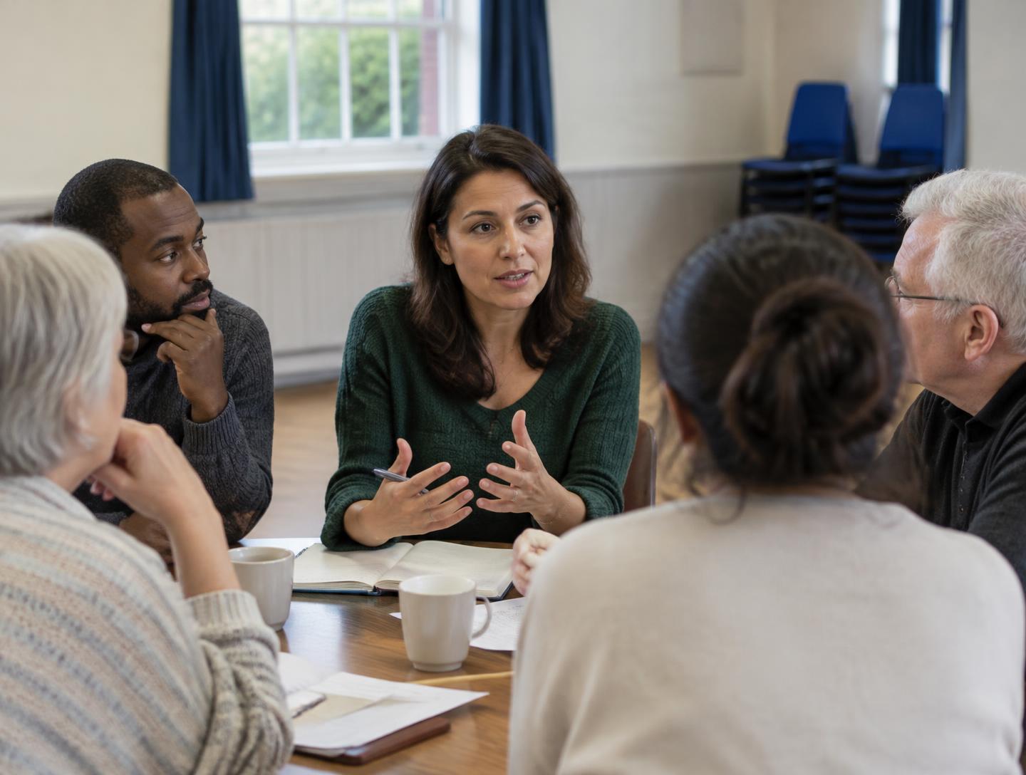 A facilitator discussing with a mixed group of adults around a workshop table.