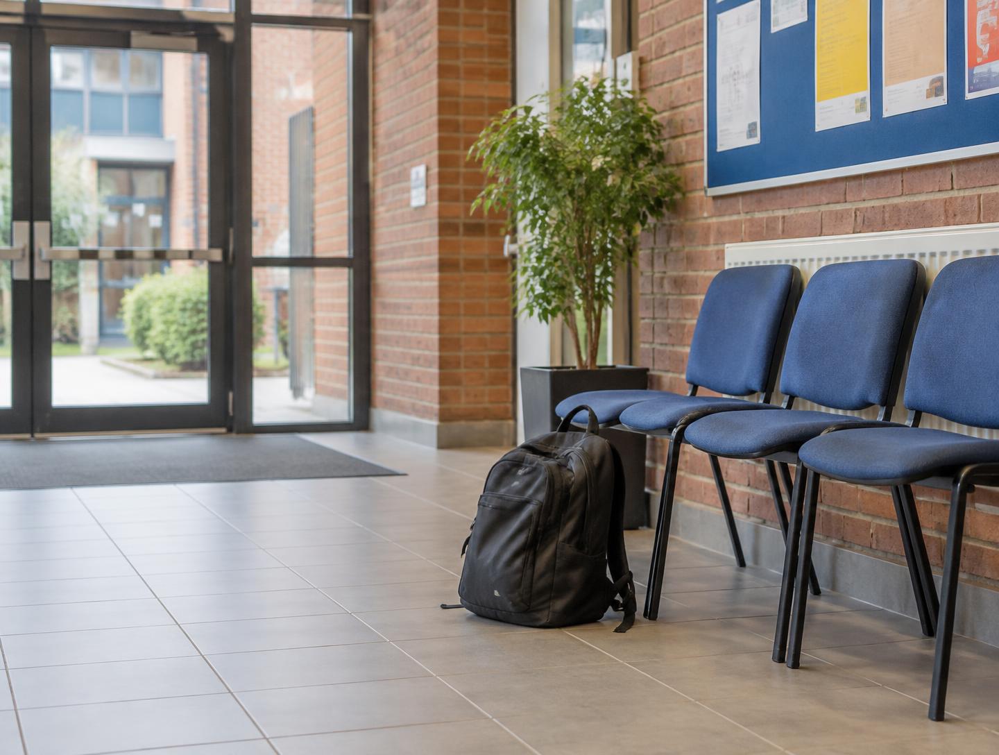 An unattended dark backpack beside a row of chairs in a community venue foyer.